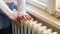 Flicka i ulltröja lägger händerna på en äldre radiator. (Bild: ©Zvone/Shutterstock.com)